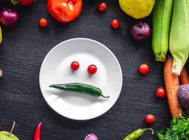 Flat lay, vegetables on a wooden background and an plate with paper. Frame of vegetables on wooden background, flat lay composition with plate in the center.